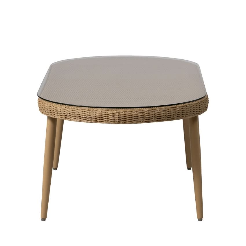 A oval outdoor cocktail table with a woven wicker frame, light beige textured top, and tapered wooden legs, shown against a plain white background.