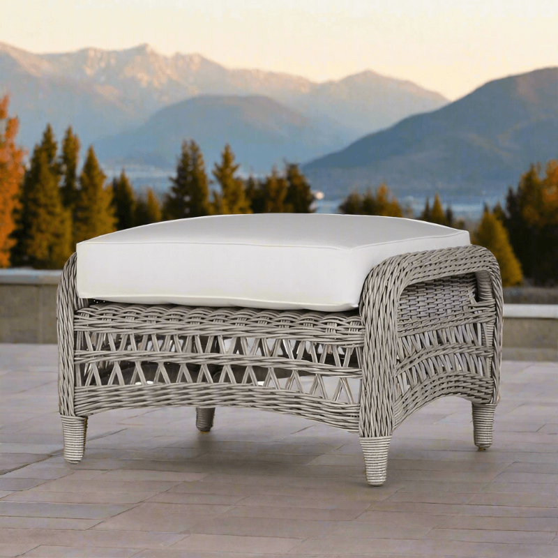 A gray Lloyd Flanders Mackinac woven vinyl ottoman with a white cushion on top, outdoor setting with mountains in the background.