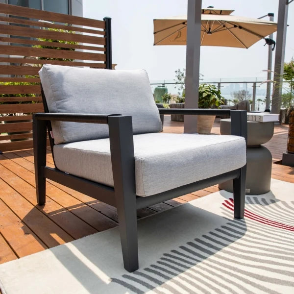 Outdoor patio lounge chair with a dark charcoal frame and light gray textured cushions, set on a striped rug on a wooden deck.