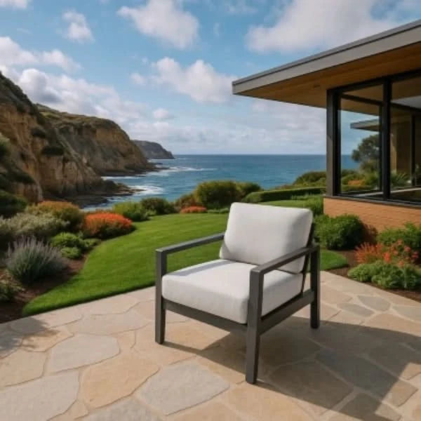 Lounge chair with white cushion on a stone patio overlooking the ocean and cliffs.