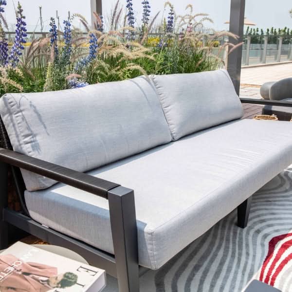 Outdoor sofa with light gray cushions and black frame on a patio with flowers in the background