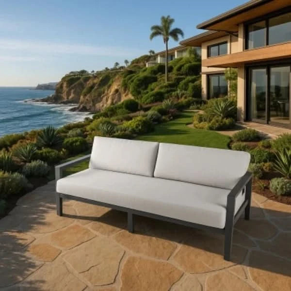 Outdoor sofa on a stone patio with ocean view and modern house in the background