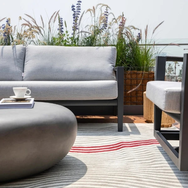 Outdoor patio set with gray sofa, coffee table, and chair on a striped rug.