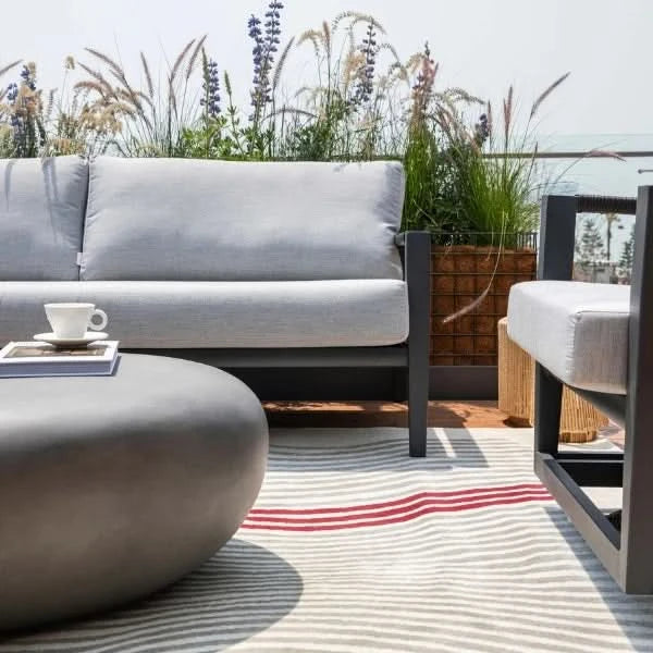 Outdoor patio set with gray sofa, coffee table, and chair on a striped rug.