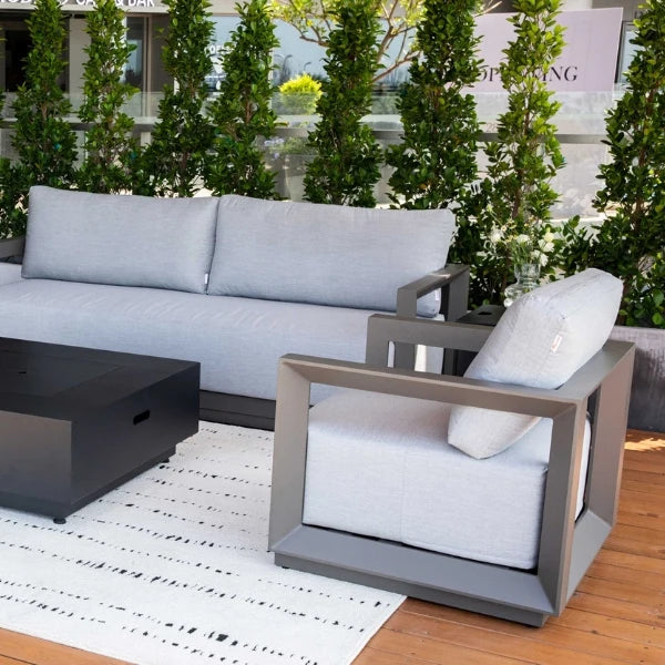 Modern outdoor patio furniture set featuring a light gray upholstered sofa and matching armchair with dark gray geometric frames, alongside a black coffee table on a white patterned rug over a wooden deck.