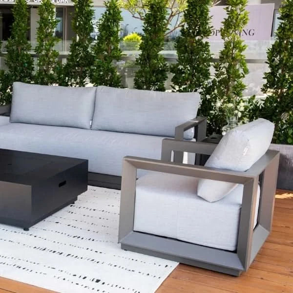 Modern outdoor patio furniture set featuring a light gray upholstered sofa and matching armchair with dark gray geometric frames, alongside a black coffee table on a white patterned rug over a wooden deck.