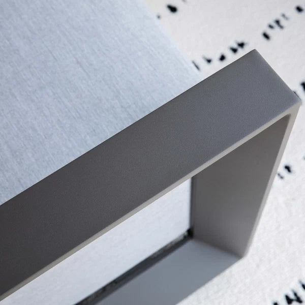 Close-up detail of a modern square outdoor chair frame in matte gray, showing the corner joint and textured light gray fabric seat on a white patterned rug.