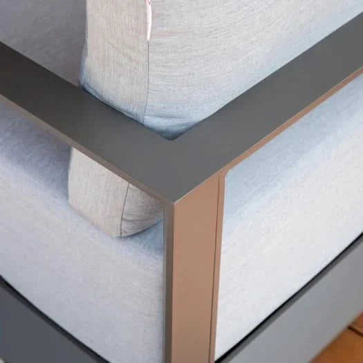 Close-up of a modern outdoor sofa corner with light gray textured fabric cushions and a dark gray metal frame with a rose gold accent leg.