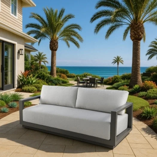 Outdoor patio with a sofa, table, and chairs overlooking the ocean with palm trees.