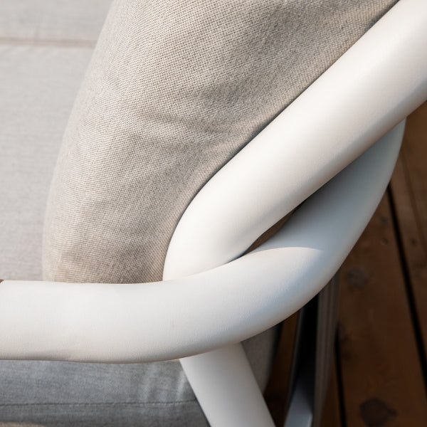 Close-up of a white curved outdoor chair frame with a light beige textured cushion and a gray seat cushion, set against a wooden deck background.