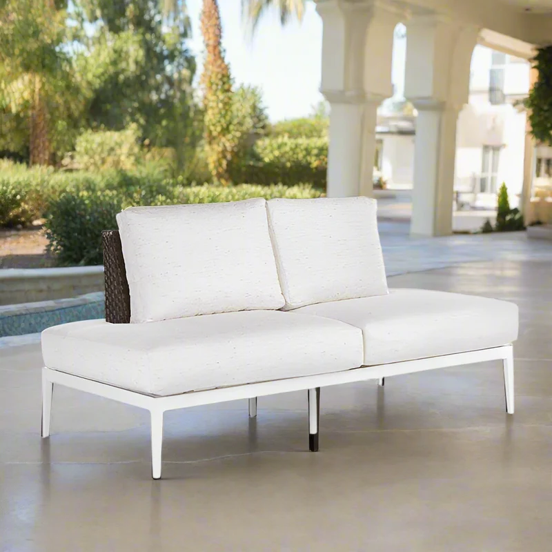White outdoor sofa with cushions on a patio with pool and garden view