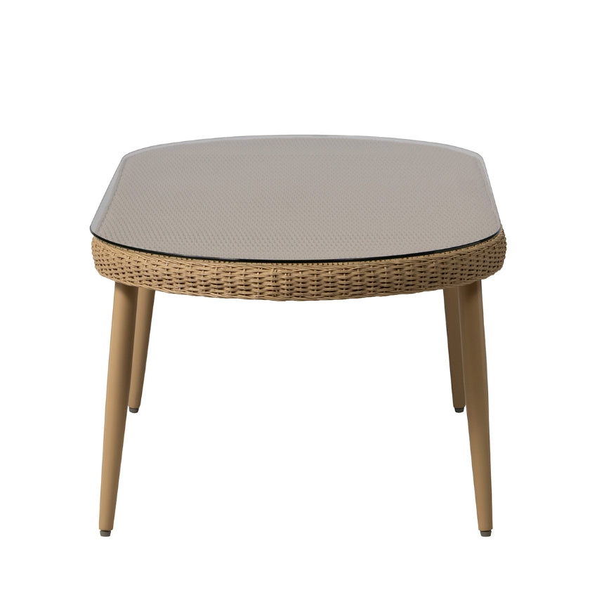 A oval outdoor cocktail table with a woven wicker frame, light beige textured top, and tapered wooden legs, shown against a plain white background.