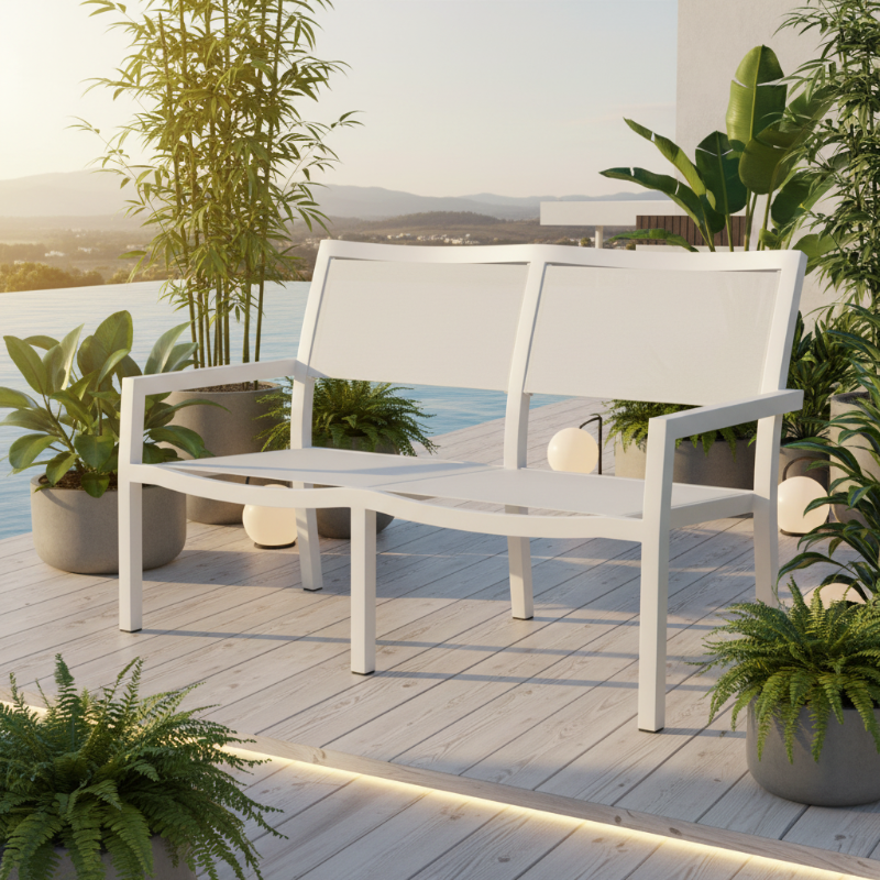 A white outdoor two-seat bench with armrests, shown on a light wood deck beside a pool with potted plants and distant hills under a warm sky.