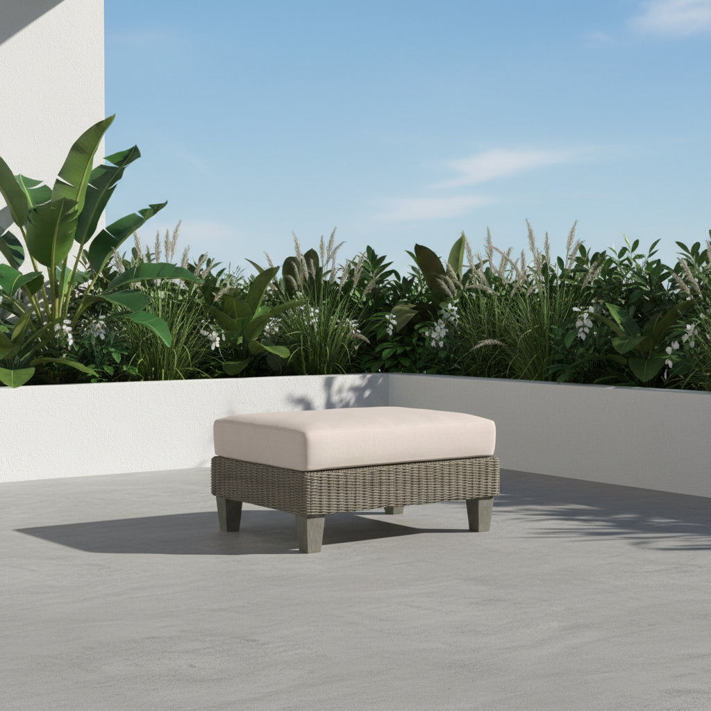 A rectangular outdoor ottoman with a light beige cushioned top and a textured gray-green woven base on short legs, shown on a plain white background.