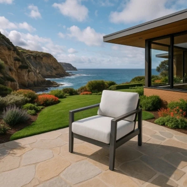 Lounge chair with white cushion on a stone patio overlooking the ocean and cliffs.
