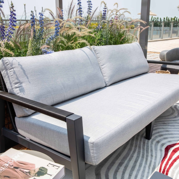 Outdoor sofa with light gray cushions and black frame on a patio with flowers in the background