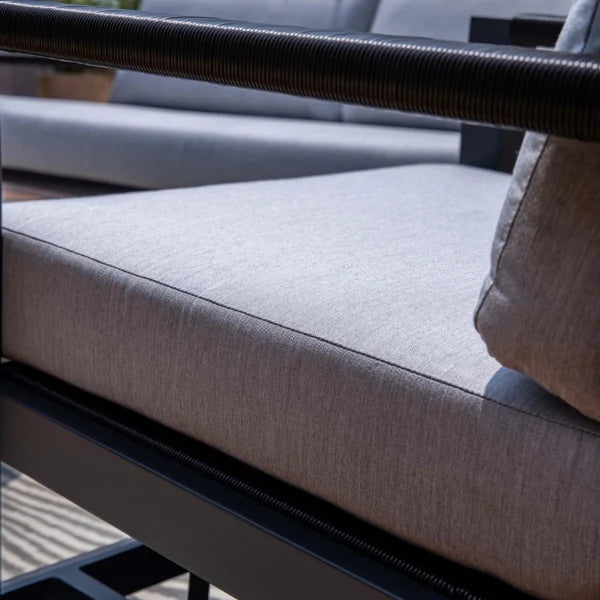 Close-up of a light gray textured outdoor patio cushion on a black aluminum frame, with part of the matching back cushion and armrest visible.