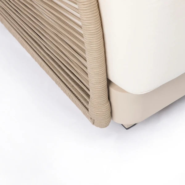Close-up detail of a modern outdoor sofa corner, showing a cream-colored seat cushion, a beige base, and a woven beige rope railing.
