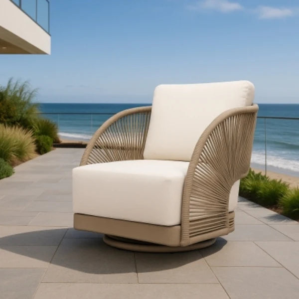 A modern outdoor swivel lounge chair with cream cushions and a woven beige frame, positioned on a tiled patio overlooking the ocean.