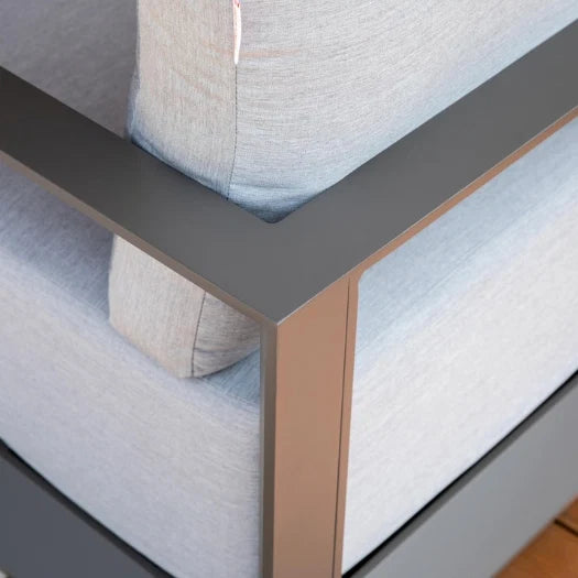 Close-up of a modern outdoor sofa corner with light gray textured fabric cushions and a dark gray metal frame with a rose gold accent leg.