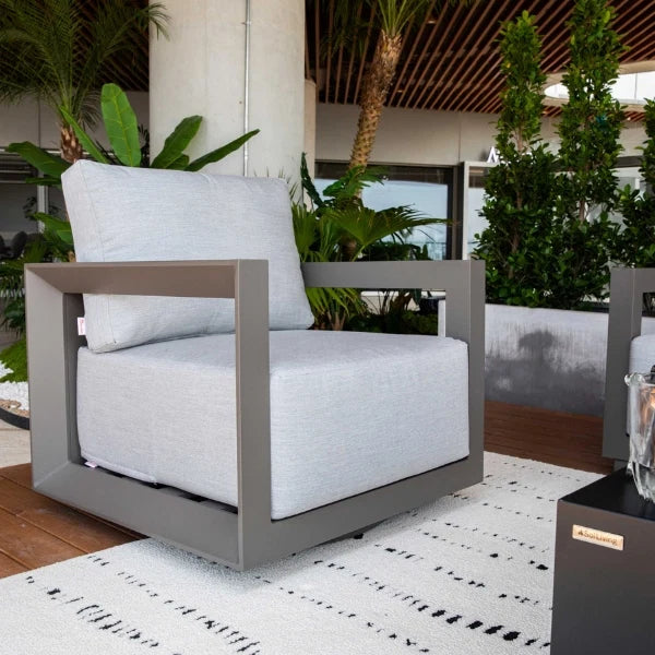 Modern outdoor swivel chair with gray frame and white cushions in a garden setting.