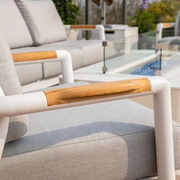 Outdoor patio chair with a light gray textured fabric cushion, a white frame, and a curved natural wood armrest, shown in a sunny patio setting next to a glass railing and pool.