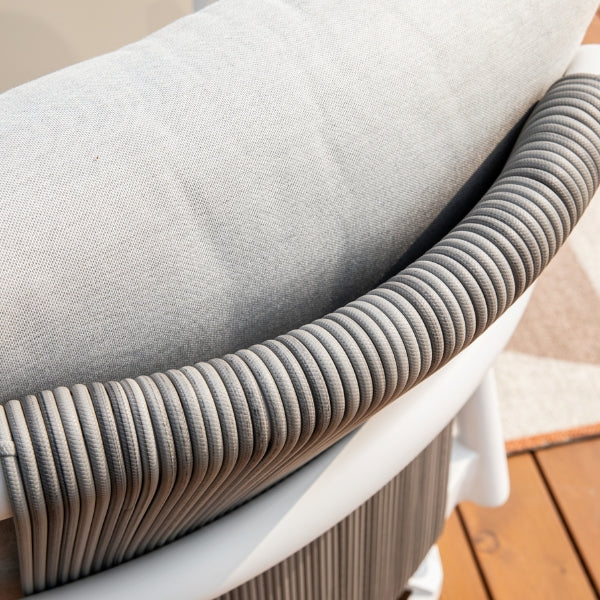 Close-up of a light gray outdoor cushion resting on a white wicker chair, set on a wooden deck.