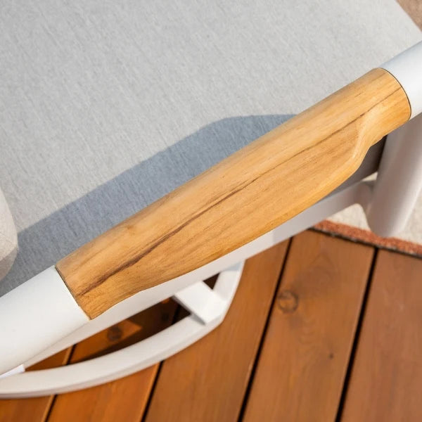 Close-up of a white outdoor patio chair with a light wood armrest and gray fabric cushion, set on a wooden deck.