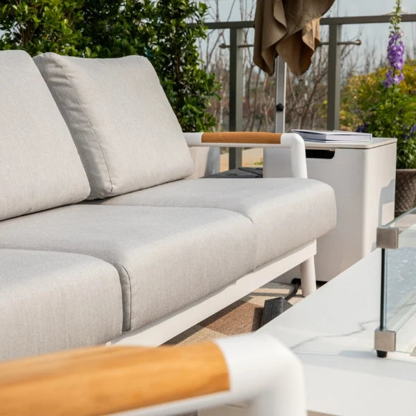Gray outdoor sofa with wooden armrests on a patio with plants and furniture in the background.