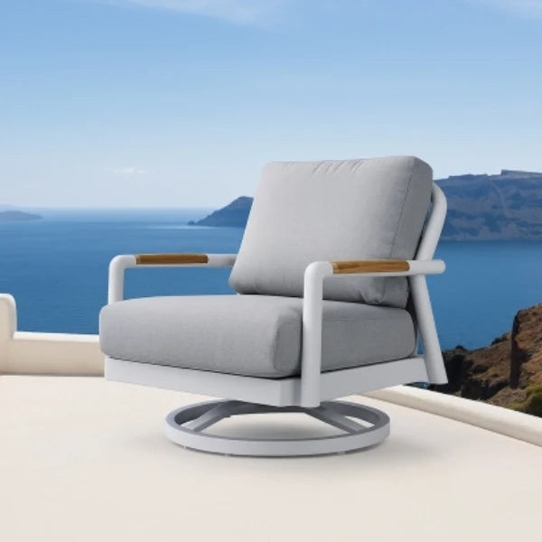 A modern outdoor swivel lounge chair with light gray cushions, a white frame, and light wood armrests, set on a patio with a scenic ocean and cliff background.