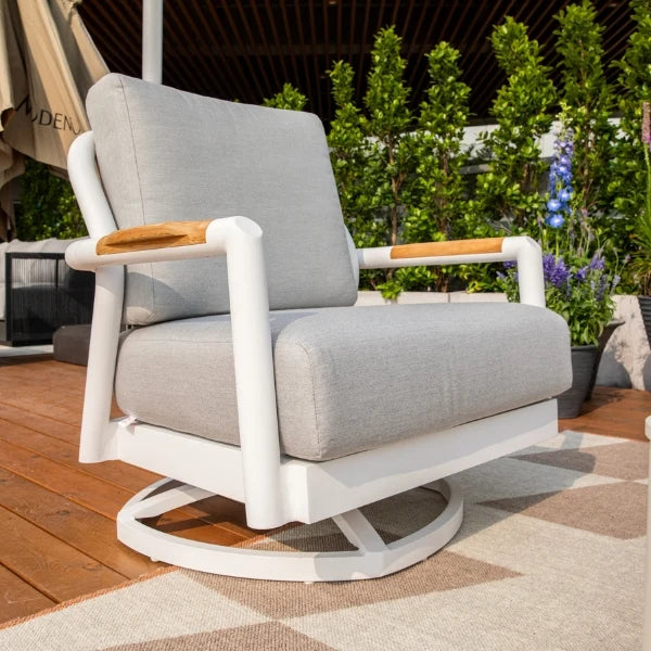 A modern outdoor swivel armchair with light gray cushions, a white frame, and light wood arm accents, shown on a patio with plants in the background.