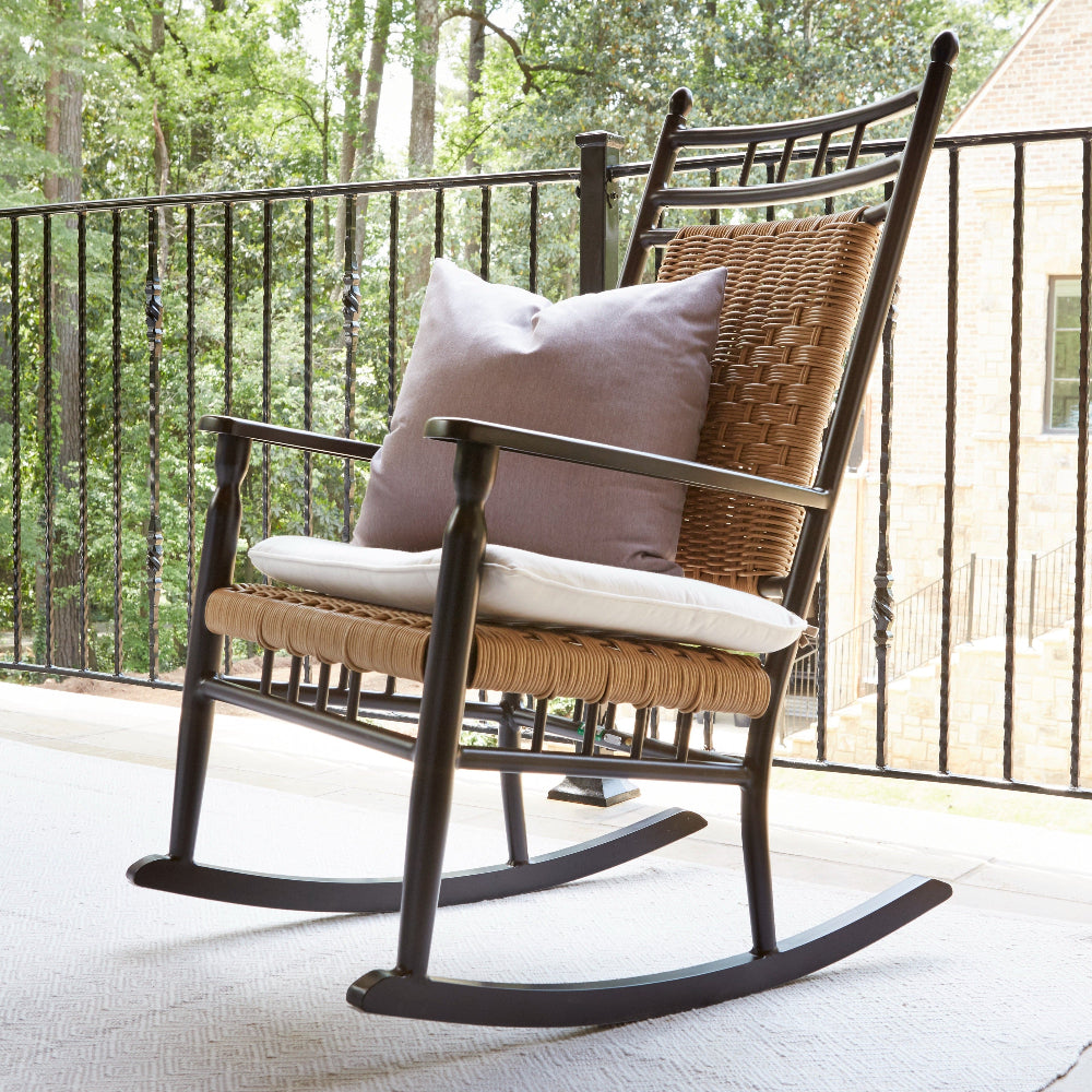 Rattan rocking chair with cushions on a patio with trees in the background